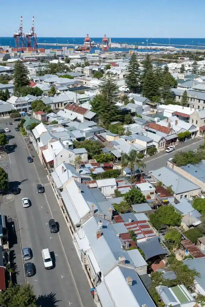 Aerial view of heritage cottages with small courtyards and patios, with port cranes and the ocean in the distance