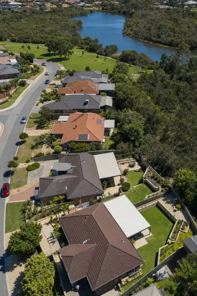 Aerial view of brick and tile homes with steel patios over their back alfrescos beside a lake and bushland