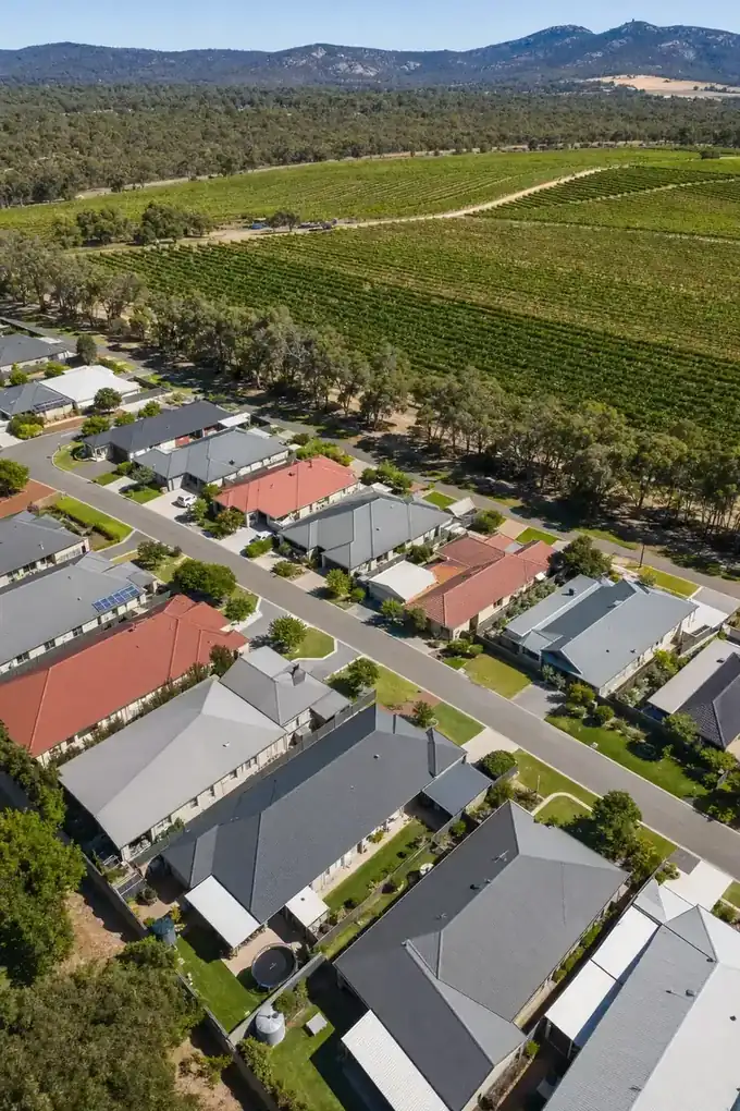 Aerial view of estate homes with steel patios beside vineyards, with the hills in the distance