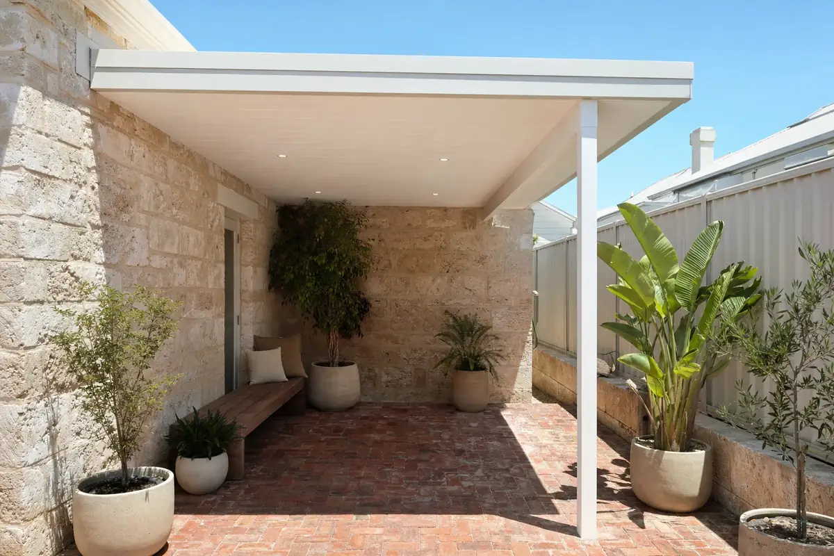 White flat roof patio with downlights over a brick-paved courtyard beside limestone walls