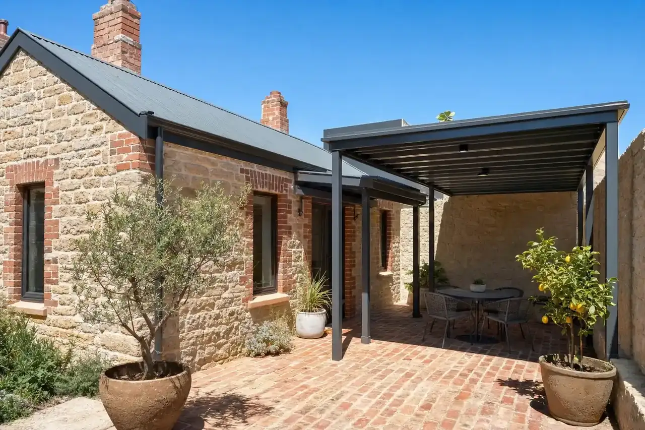 Charcoal skillion patio over a brick-paved courtyard behind a limestone and brick cottage