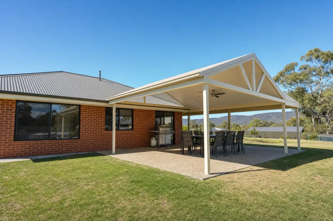 Cream gable patio with a fan over a concrete alfresco at a red brick home with hills in the distance