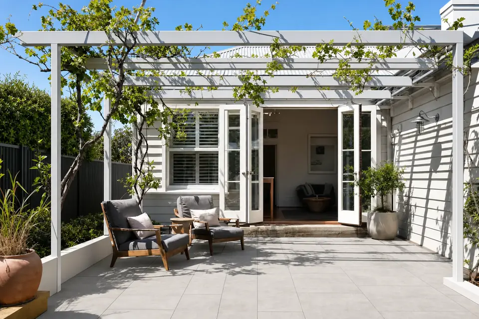 White steel pergola over stone-look paving with a young grapevine climbing the frame at a Perth home