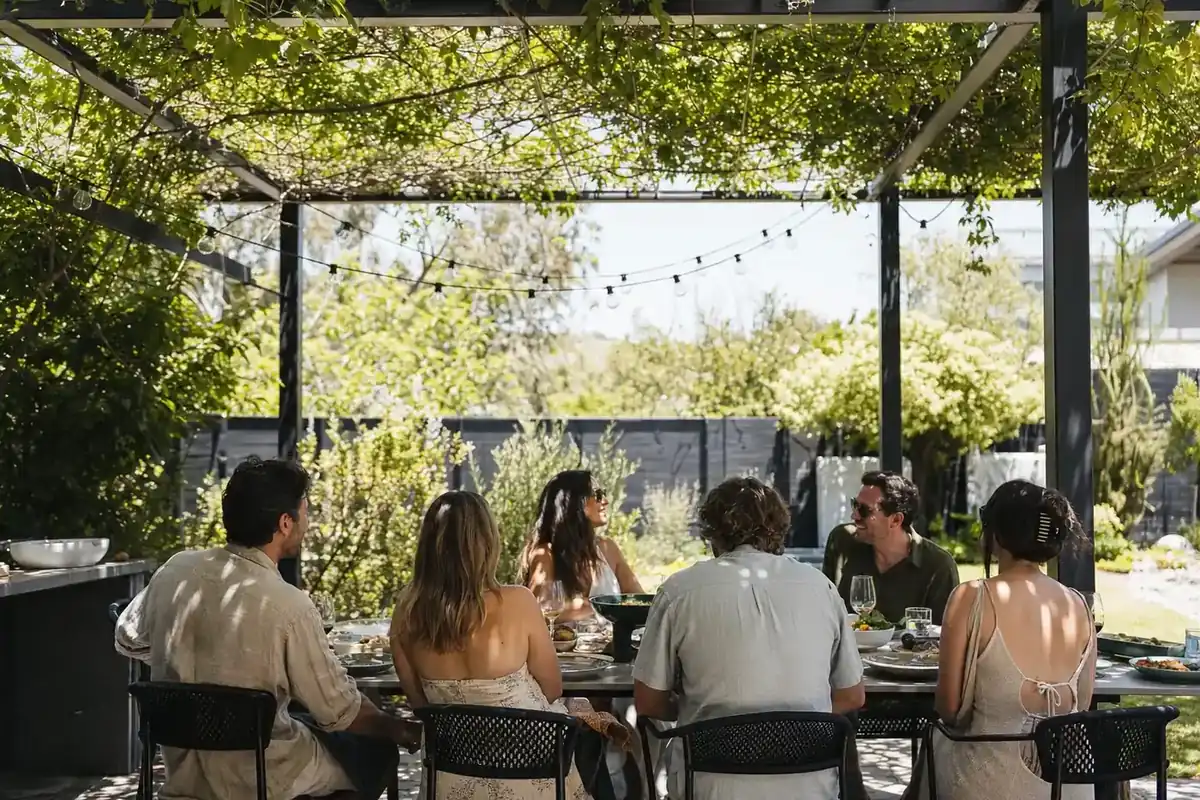 Friends at an outdoor table under a vine-covered steel pergola in a Perth backyard