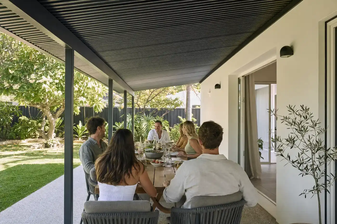 Friends sharing lunch at a long table under a charcoal skillion patio in a Perth backyard